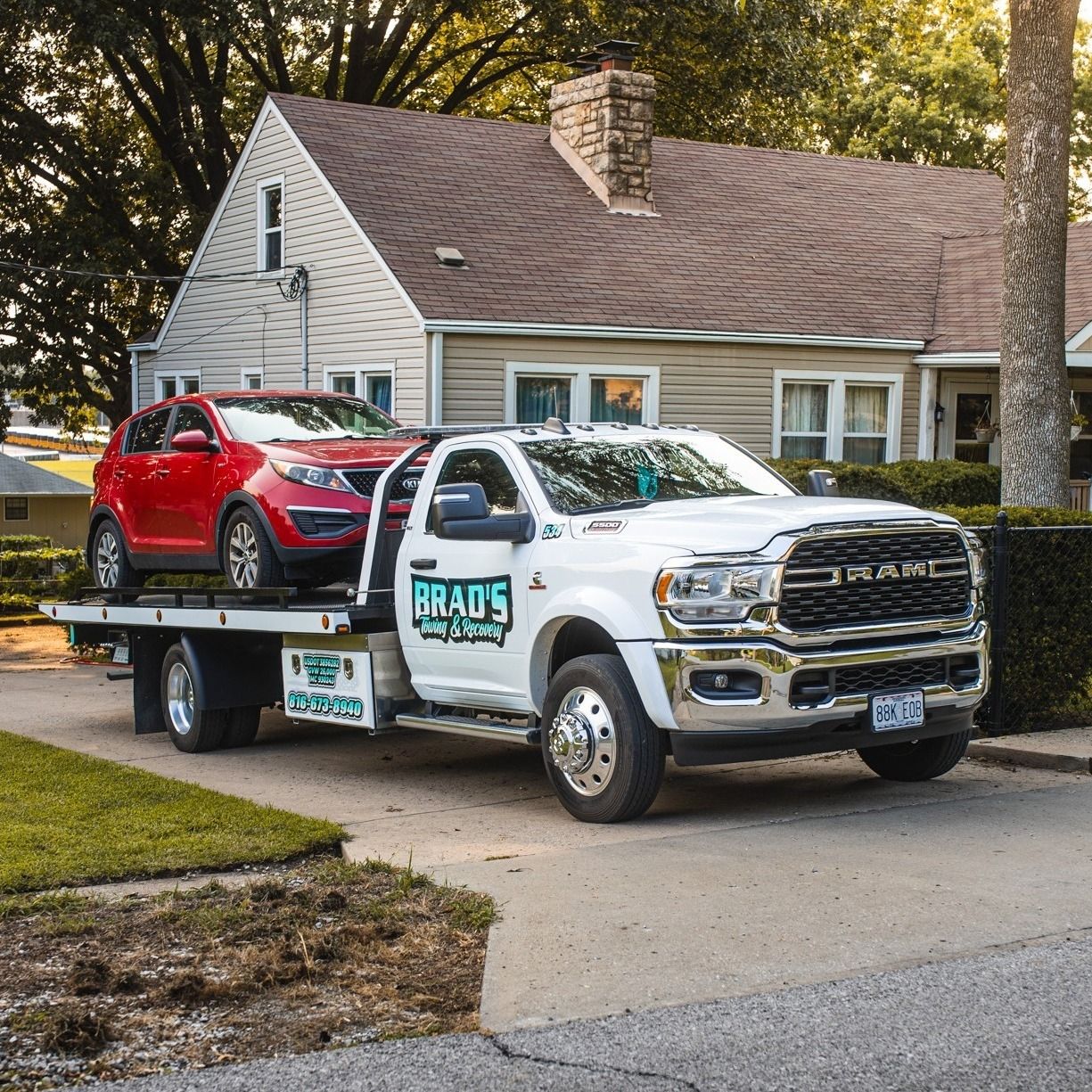 A white tow truck with two cars on the back is parked in front of a house.