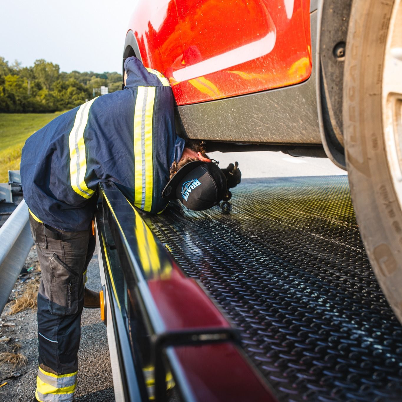 Tow truck operator works on a red car on a flatbed truck, roadside.