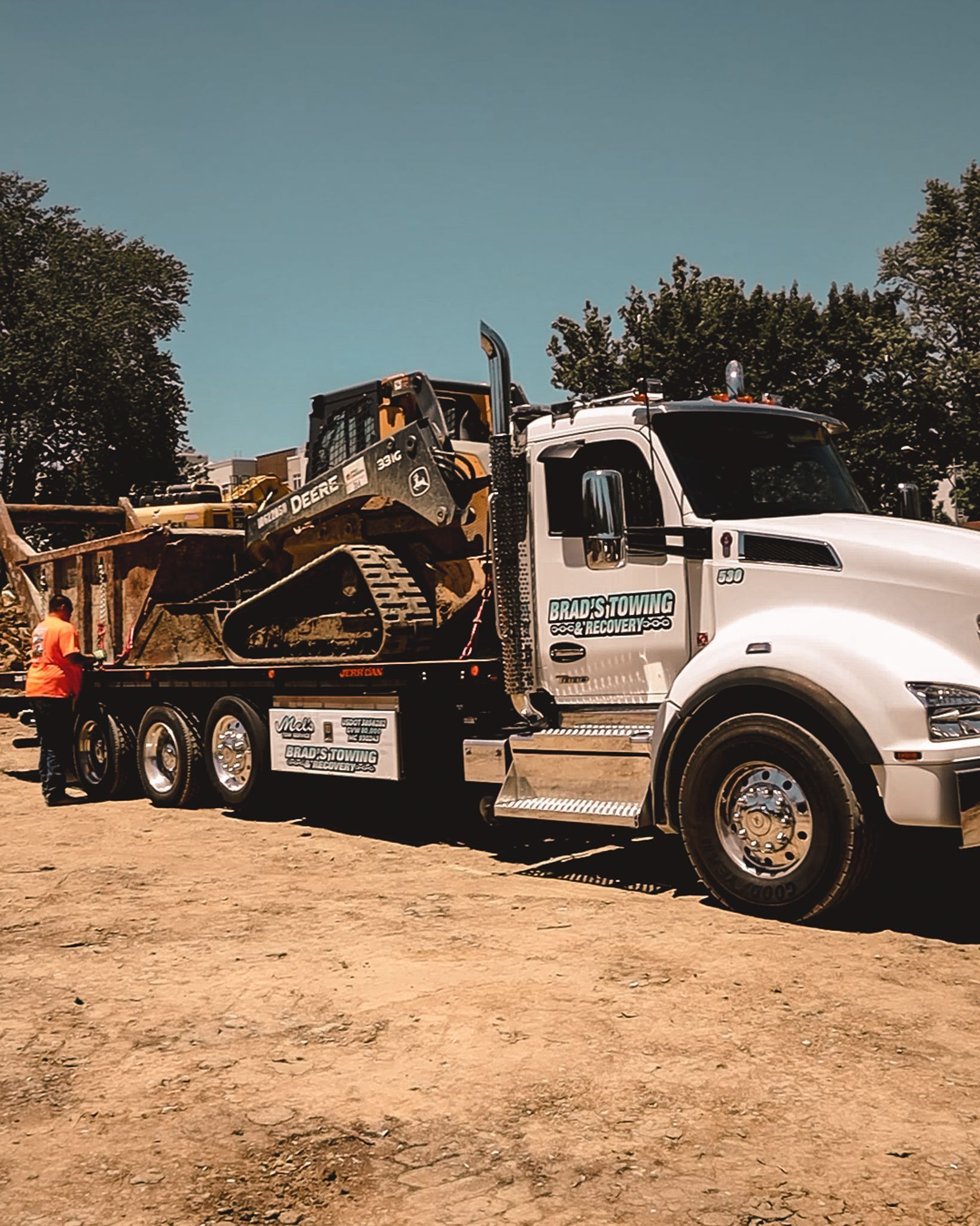 A white semi truck is carrying a bulldozer on the back of it.