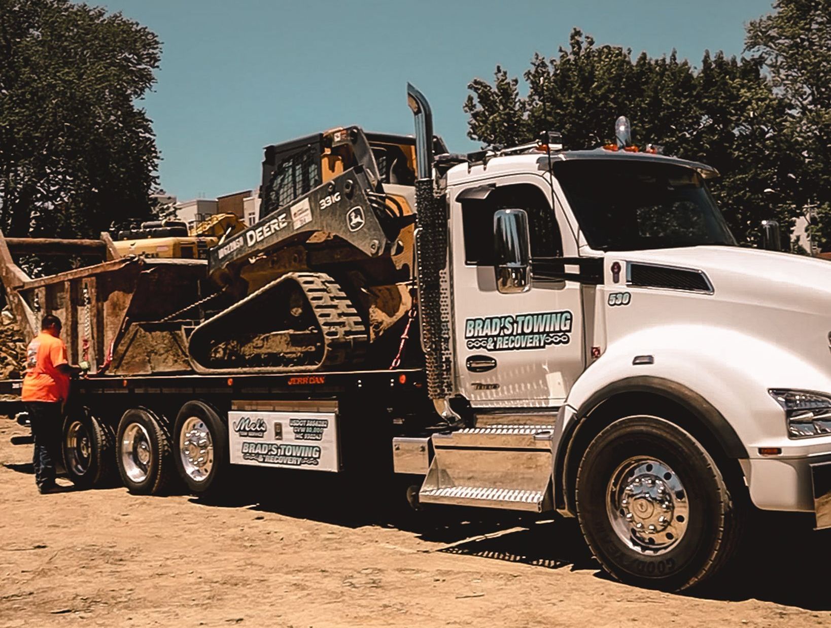 A white truck is carrying a bulldozer on the back of it.
