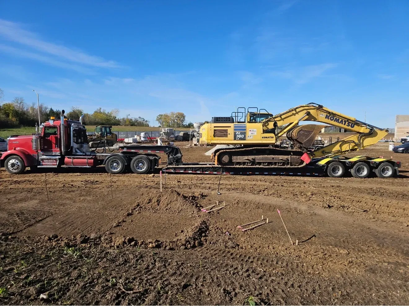 A specialized low boy RGN trailer transporting heavy industrial machinery and a Connex storage box through Raytown Missouri.