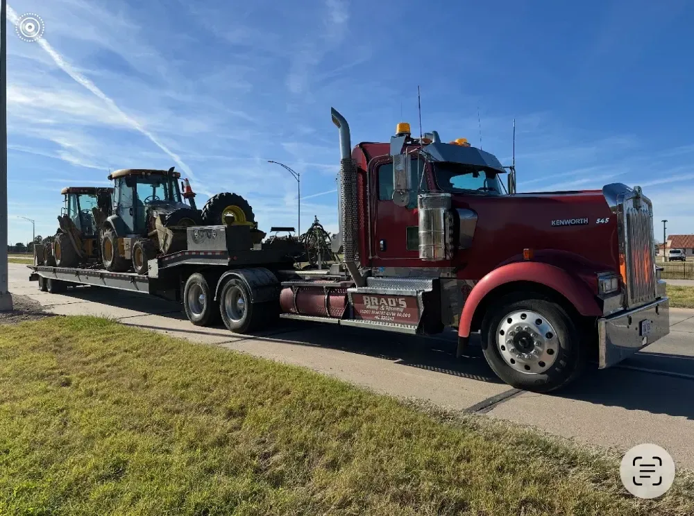 A specialized low boy RGN trailer transporting heavy machinery and a Connex container past the Crossroads District in Downtown KC.