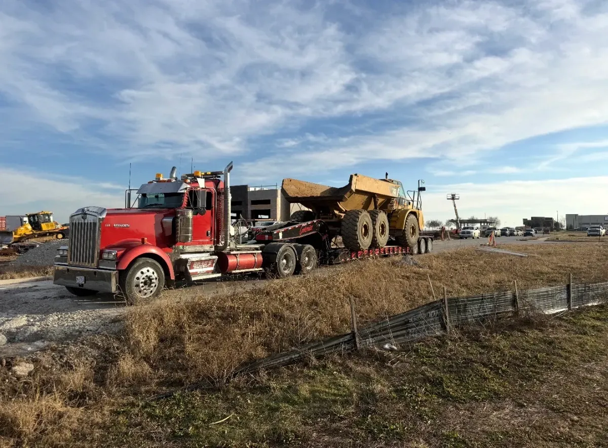 A specialized low boy RGN trailer transporting heavy industrial machinery and a Connex container through St. Joe Missouri.