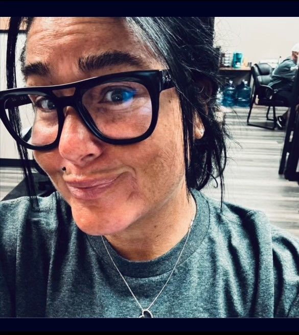 A woman wearing glasses and a necklace is smiling for the camera