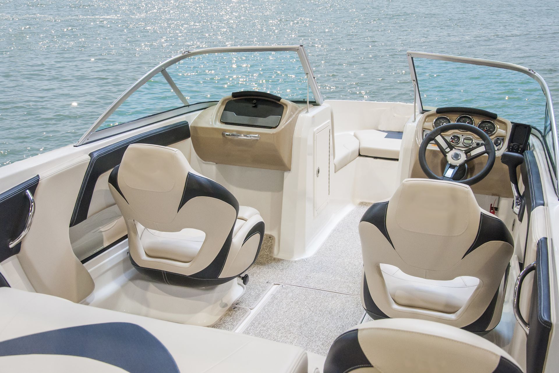 Boat cockpit with tan seats, steering wheel, and windshield overlooking blue water.
