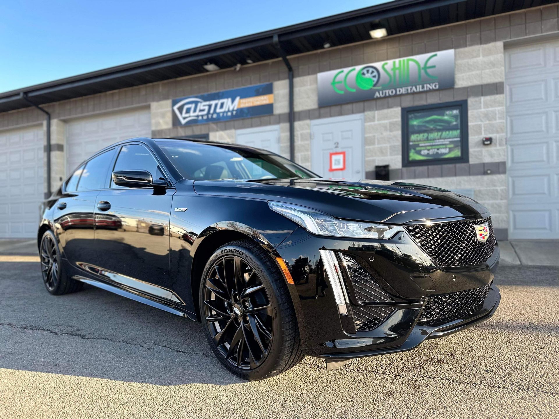 Black sedan parked outside an auto shop with a gray cinderblock building in the background