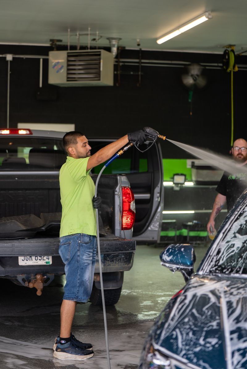 Two people washing a black truck in a garage, spraying water across the vehicle