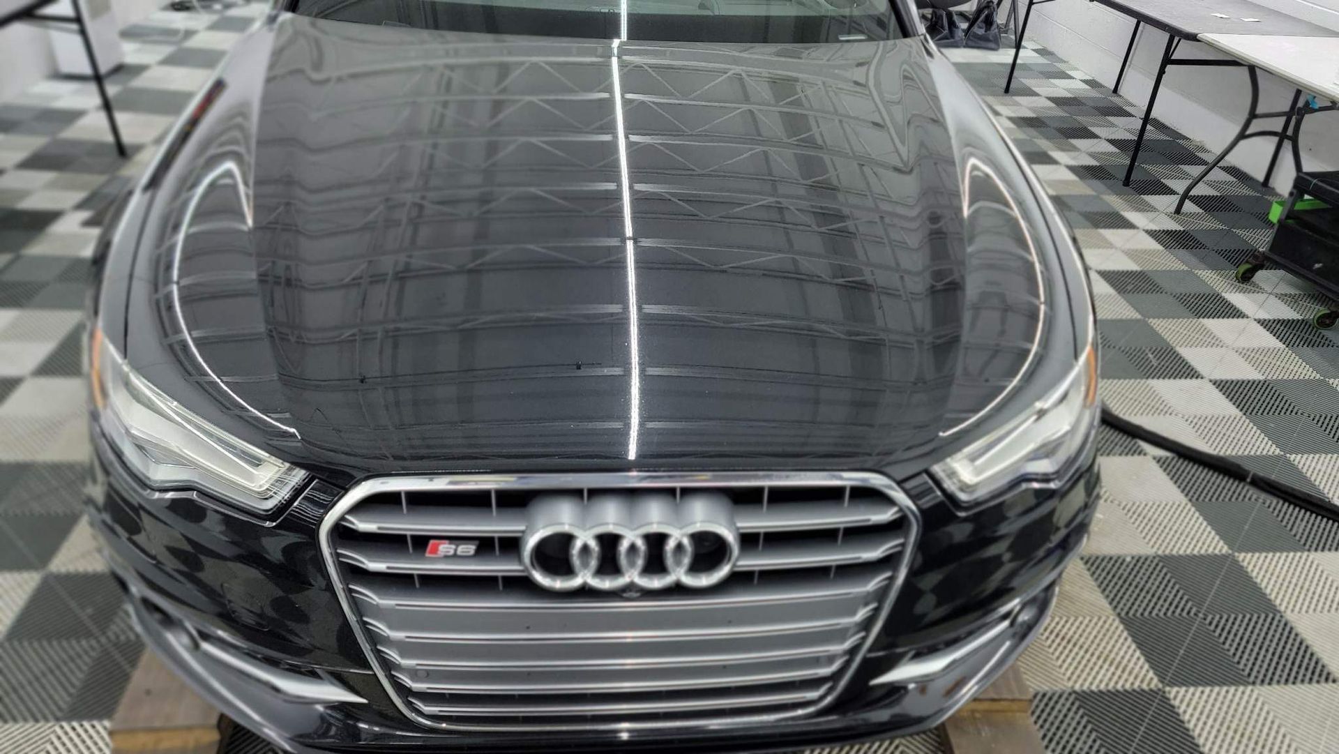 Front view of a black Audi sedan in a showroom, with a checkered floor and bright overhead lights.