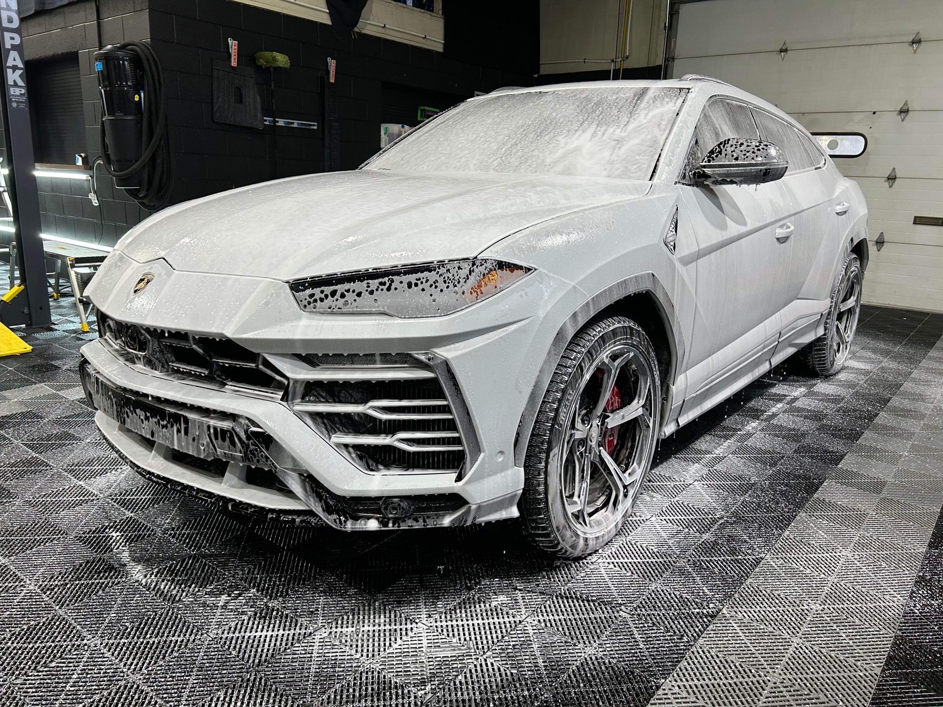 White SUV covered in foam in an indoor car wash, viewed from the front-left side.