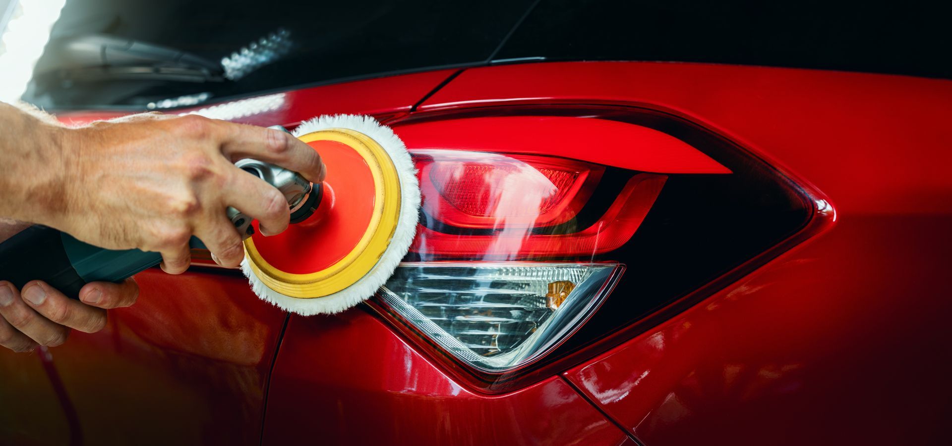Hand polishing a red car’s taillight with a buffer.