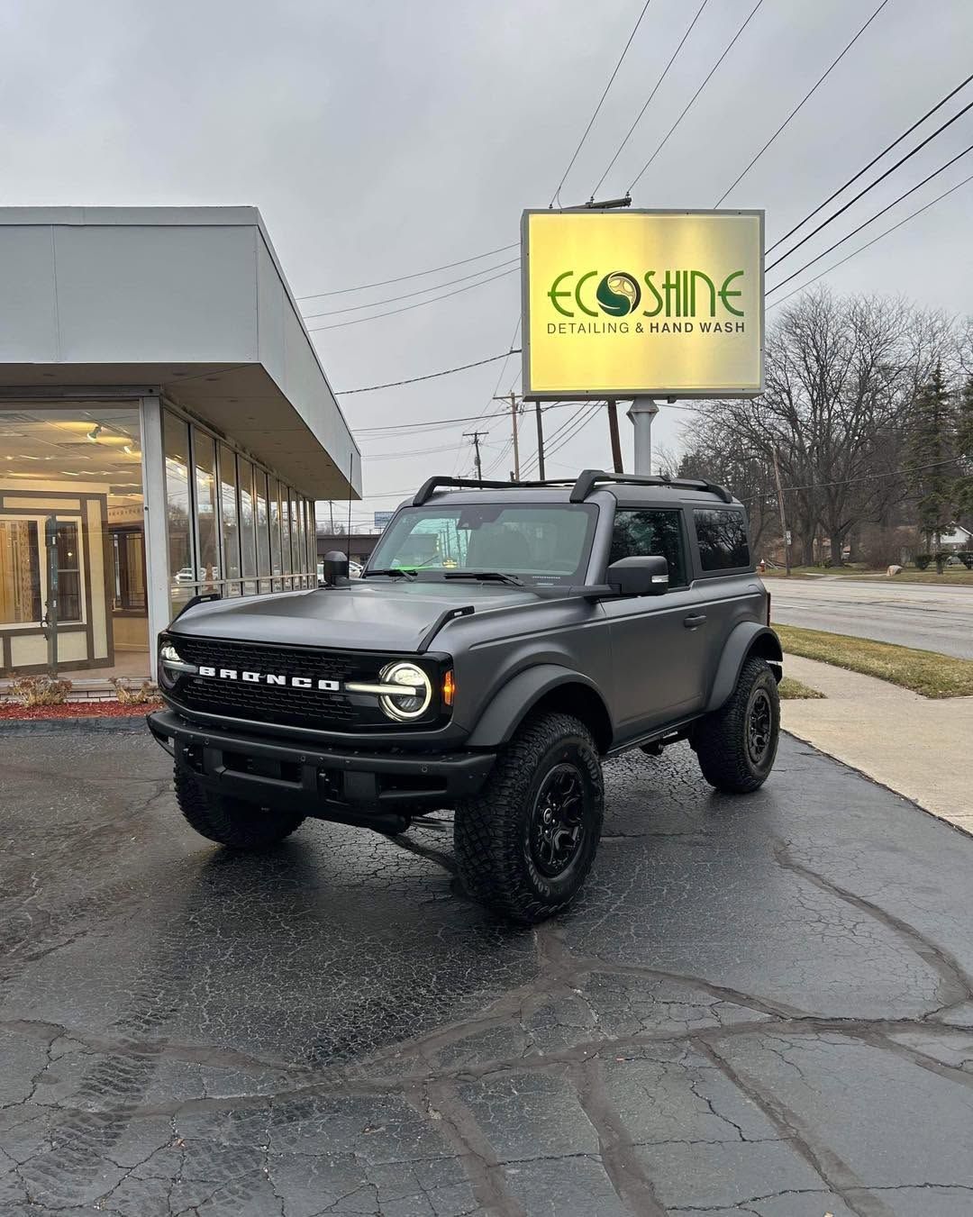Black lifted SUV parked outside an eco-side dealership on a wet day