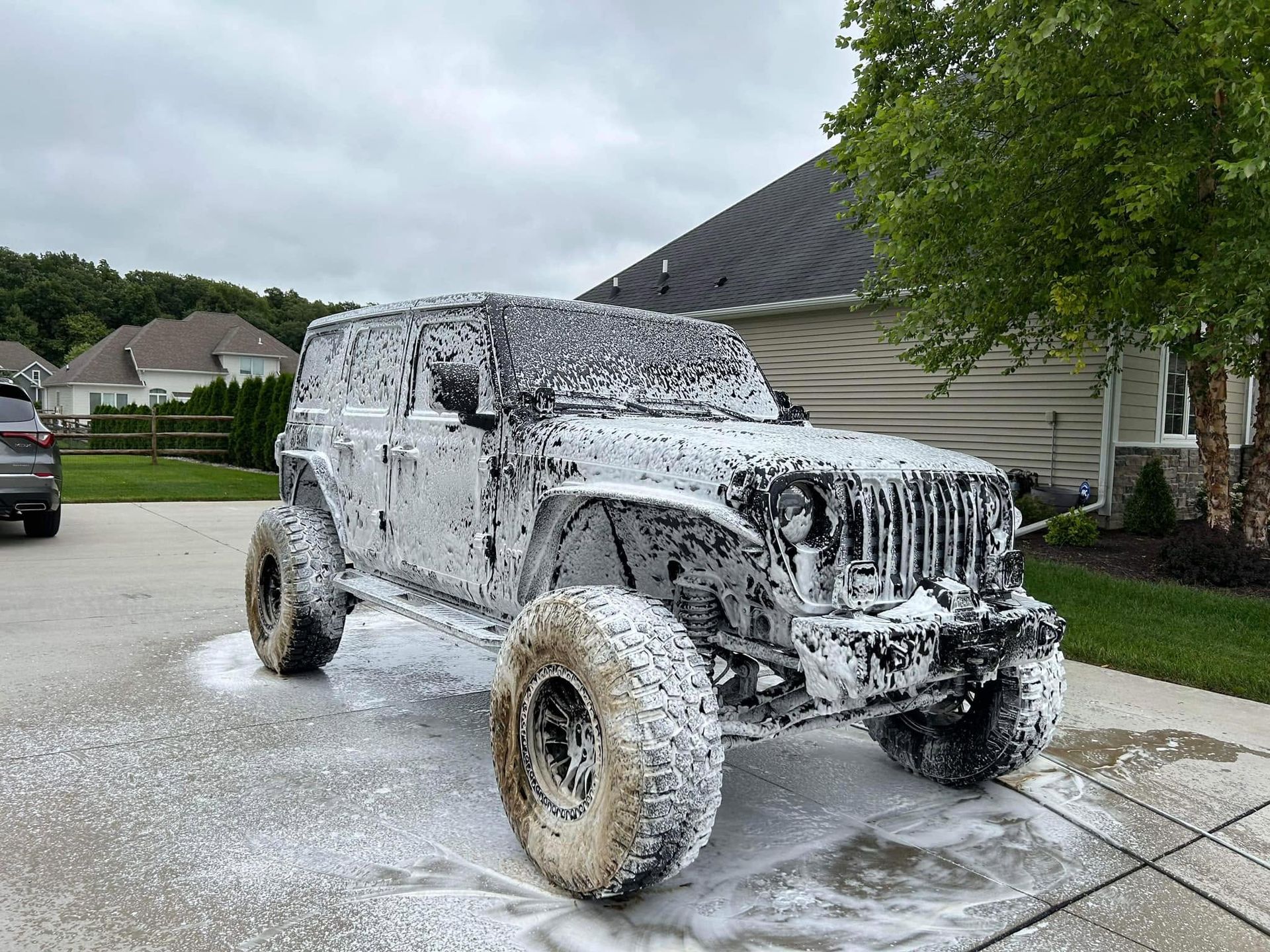 White Jeep covered in soap foam being washed in a suburban driveway
