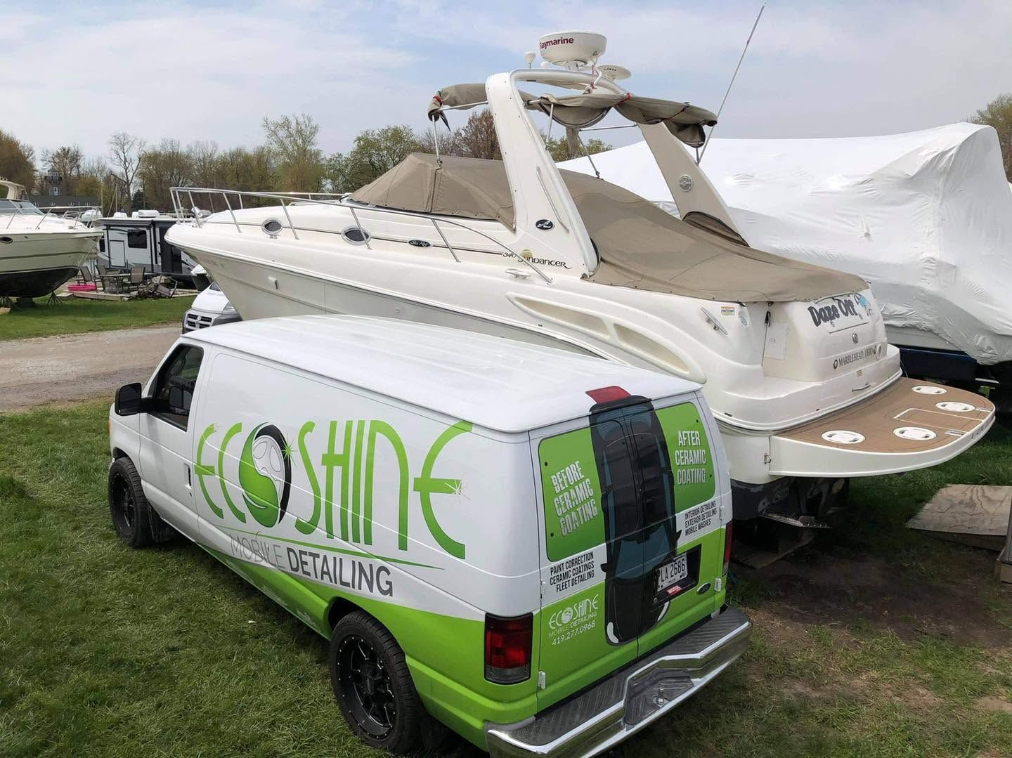 White van with green “LoSHINE” logo parked beside a boat on a trailer in a grassy outdoor lot