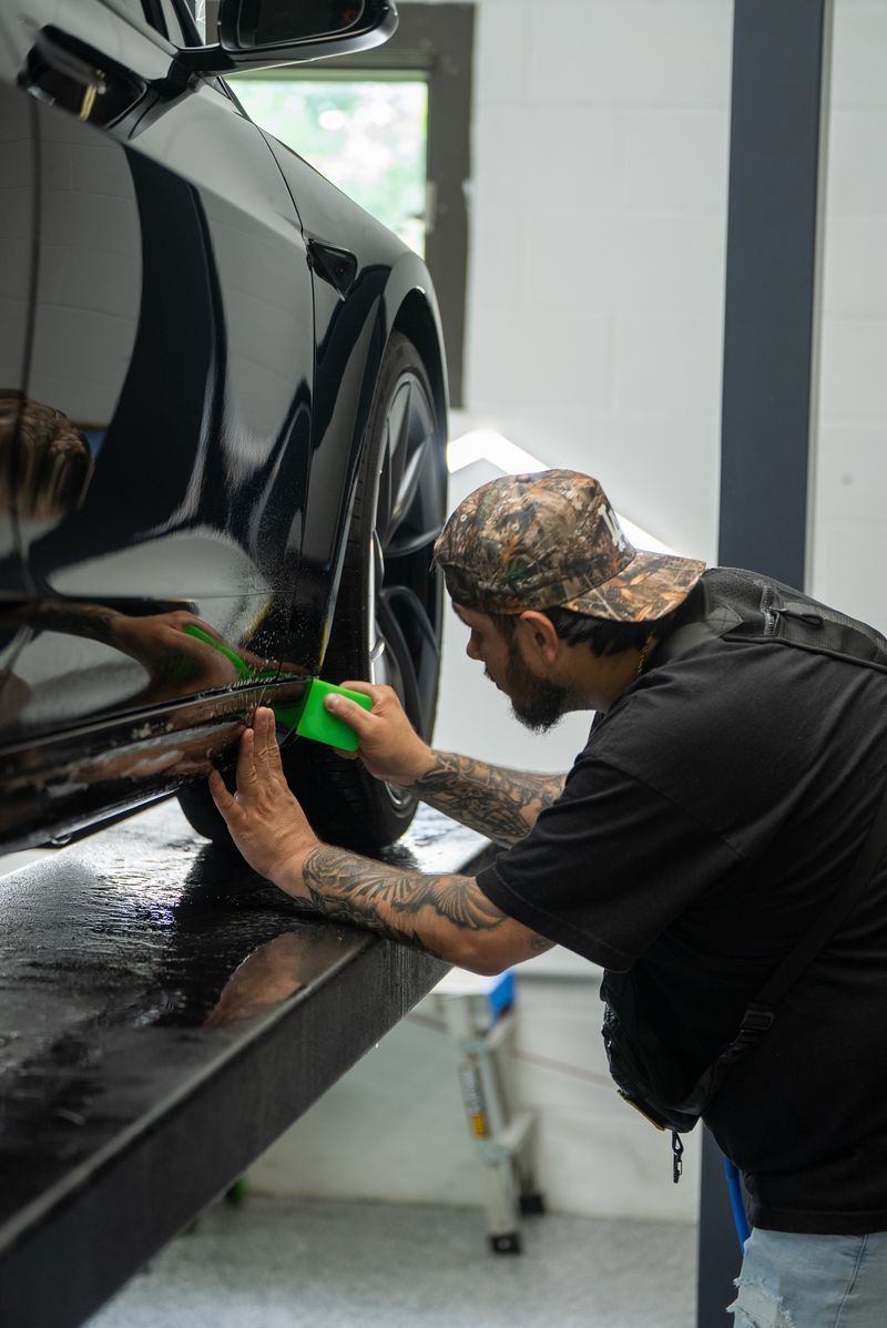Person hand-polishing a black car door with a green cloth in a garage