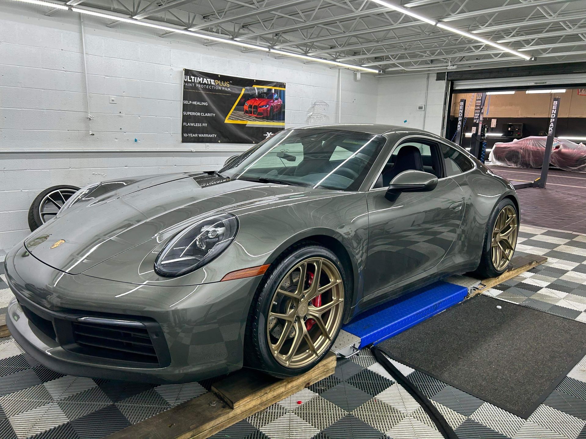 Gray Porsche sports car on a dyno in a workshop, with gold wheels and black roof.