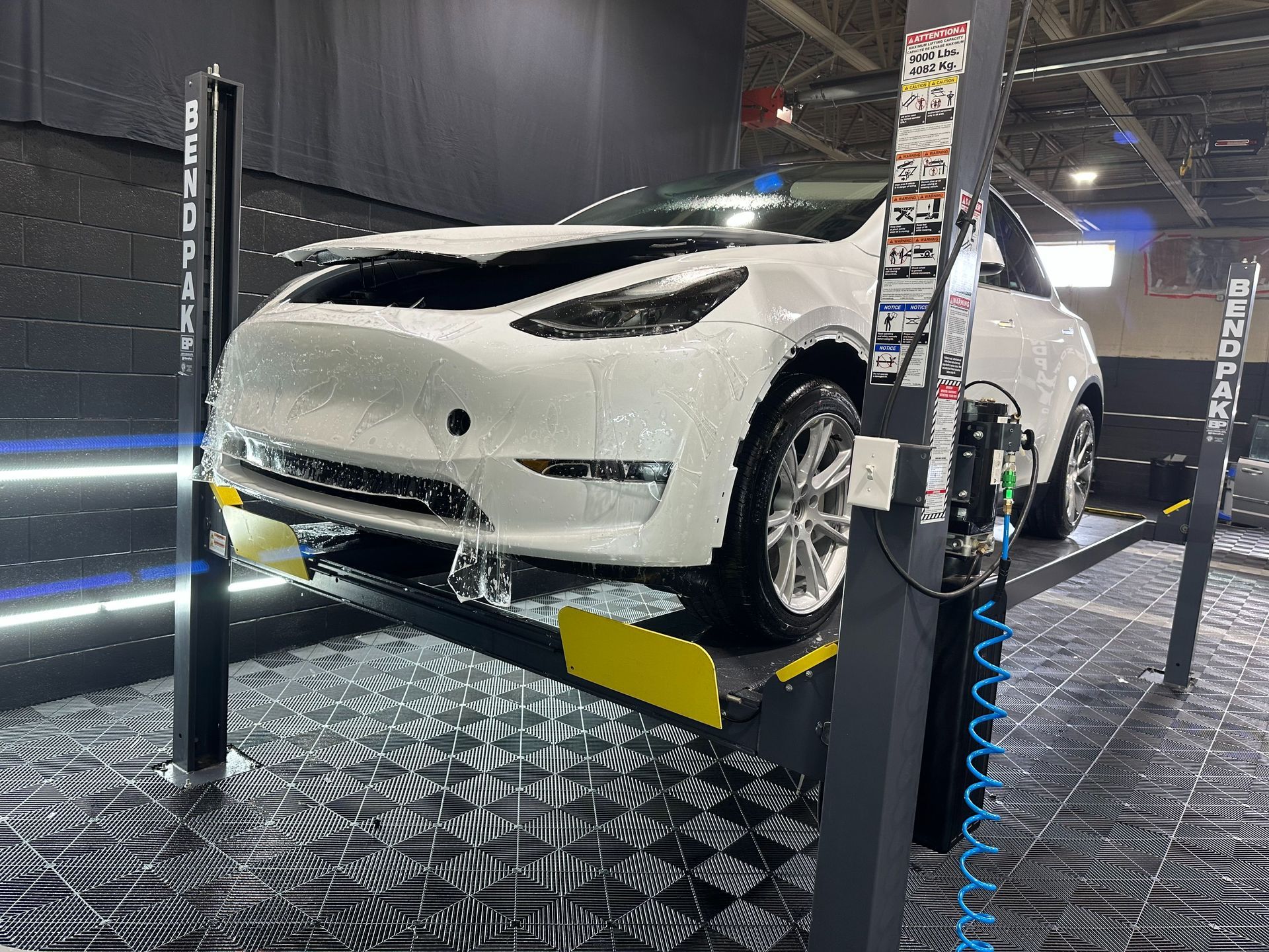 White car on a hydraulic lift in an auto shop, viewed from the front.