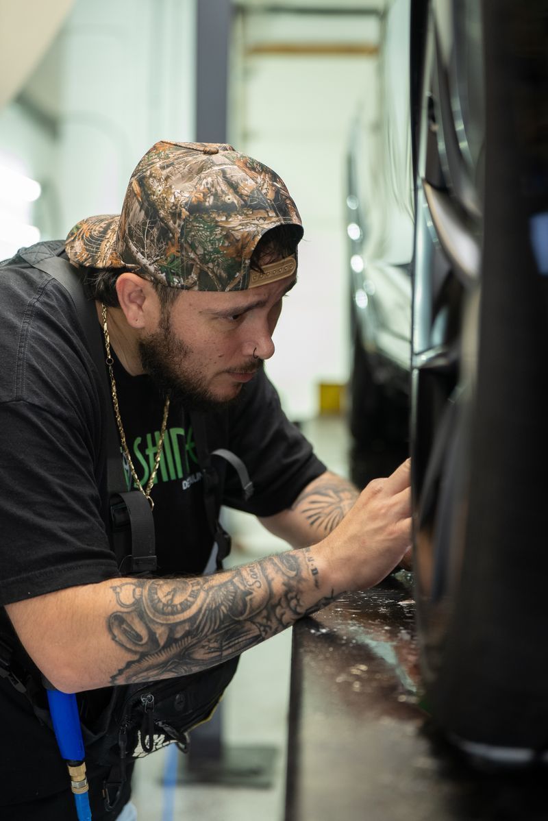 Man in a camo cap crouches and works on a black car in a garage.