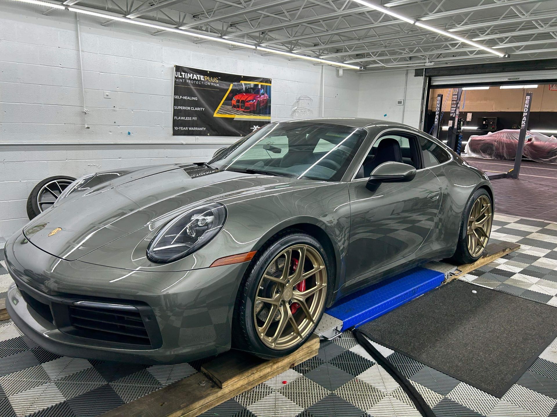 Gray Porsche 911 on a dyno in a garage, with gold wheels and blue roller platform