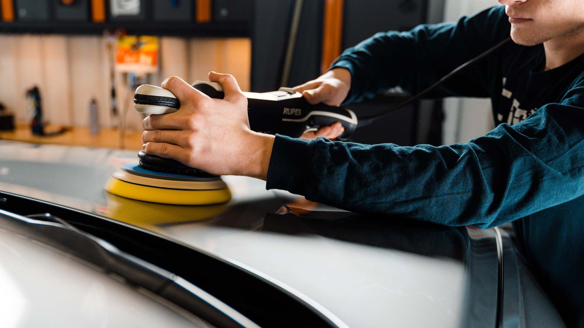 Man in a camo cap crouches and works on a black car in a garage.