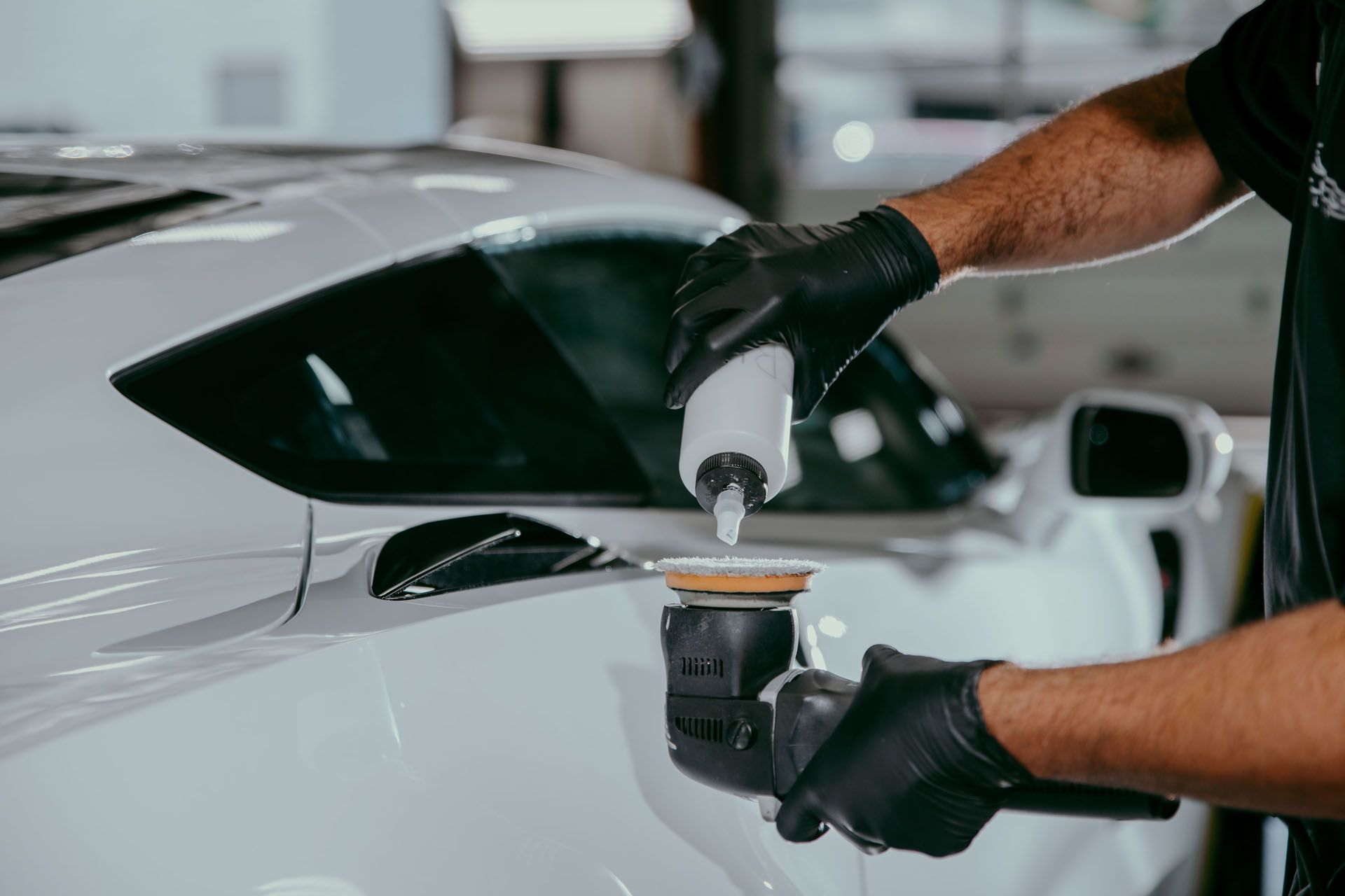 Detailing a black car with a green sponge in a workshop