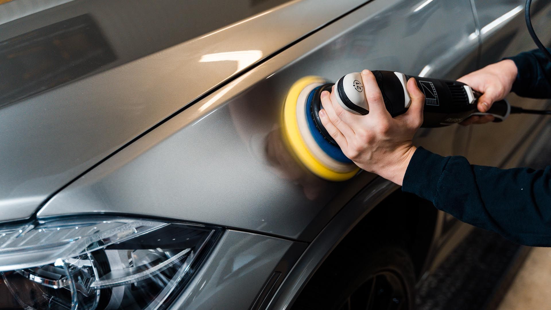 Person polishing a black car hood with a power buffer, creating a glossy shine.