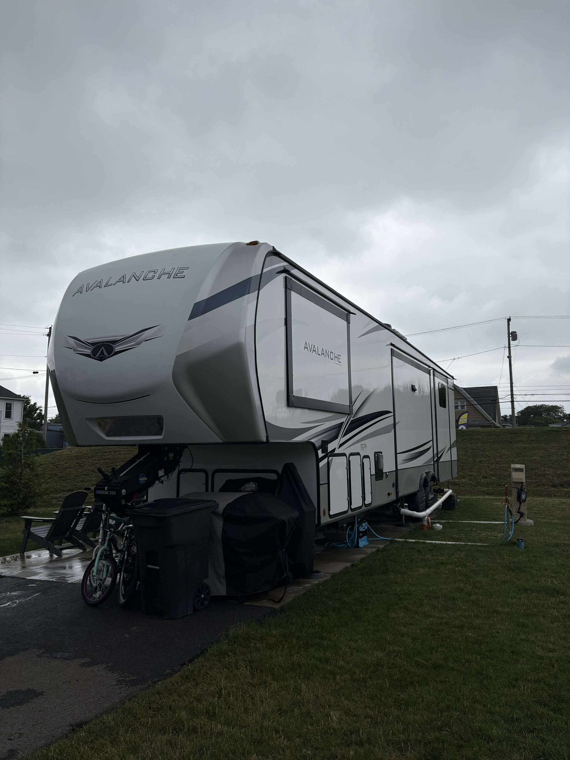 Large white fifth-wheel RV trailer parked on a grassy roadside under a cloudy sky.