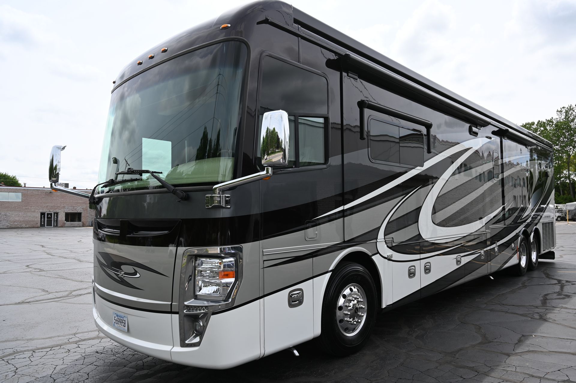 Black and silver luxury motorcoach parked in a lot, angled front view