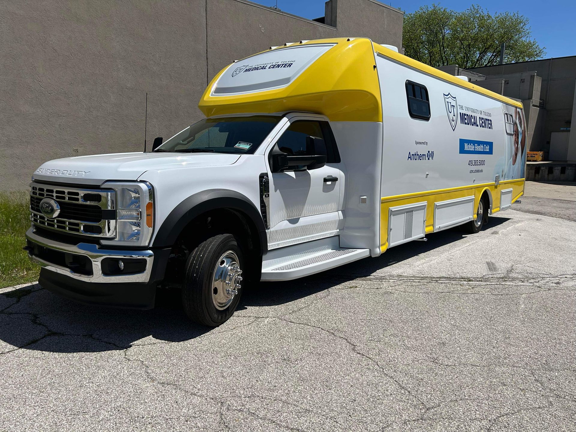 White and yellow utility truck parked outdoors beside a building, with company signage on the side