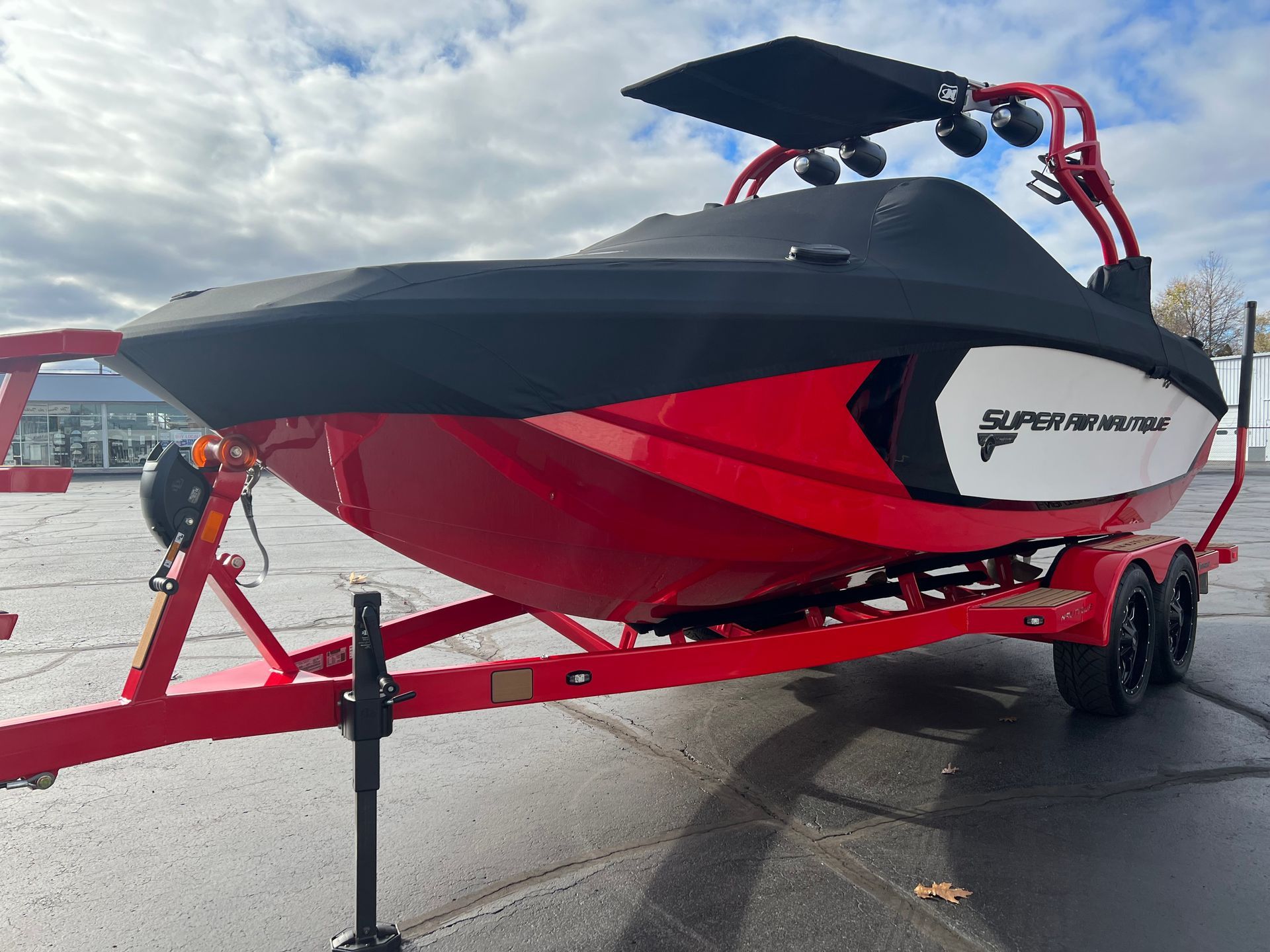 Red and black Nautique boat on a trailer at a boat ramp, with a bimini top raised on deck.