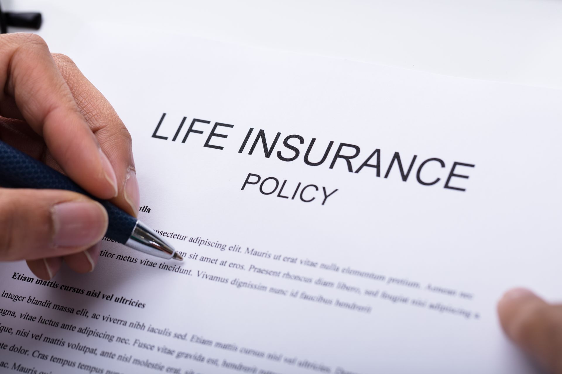 Hand holding a pen, signing a life insurance policy document.