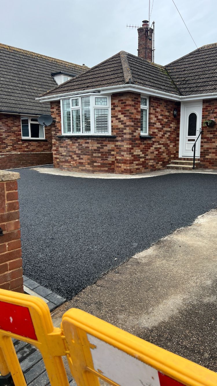 Permeable tarmac driveway in the front garden of a red bungalow.
