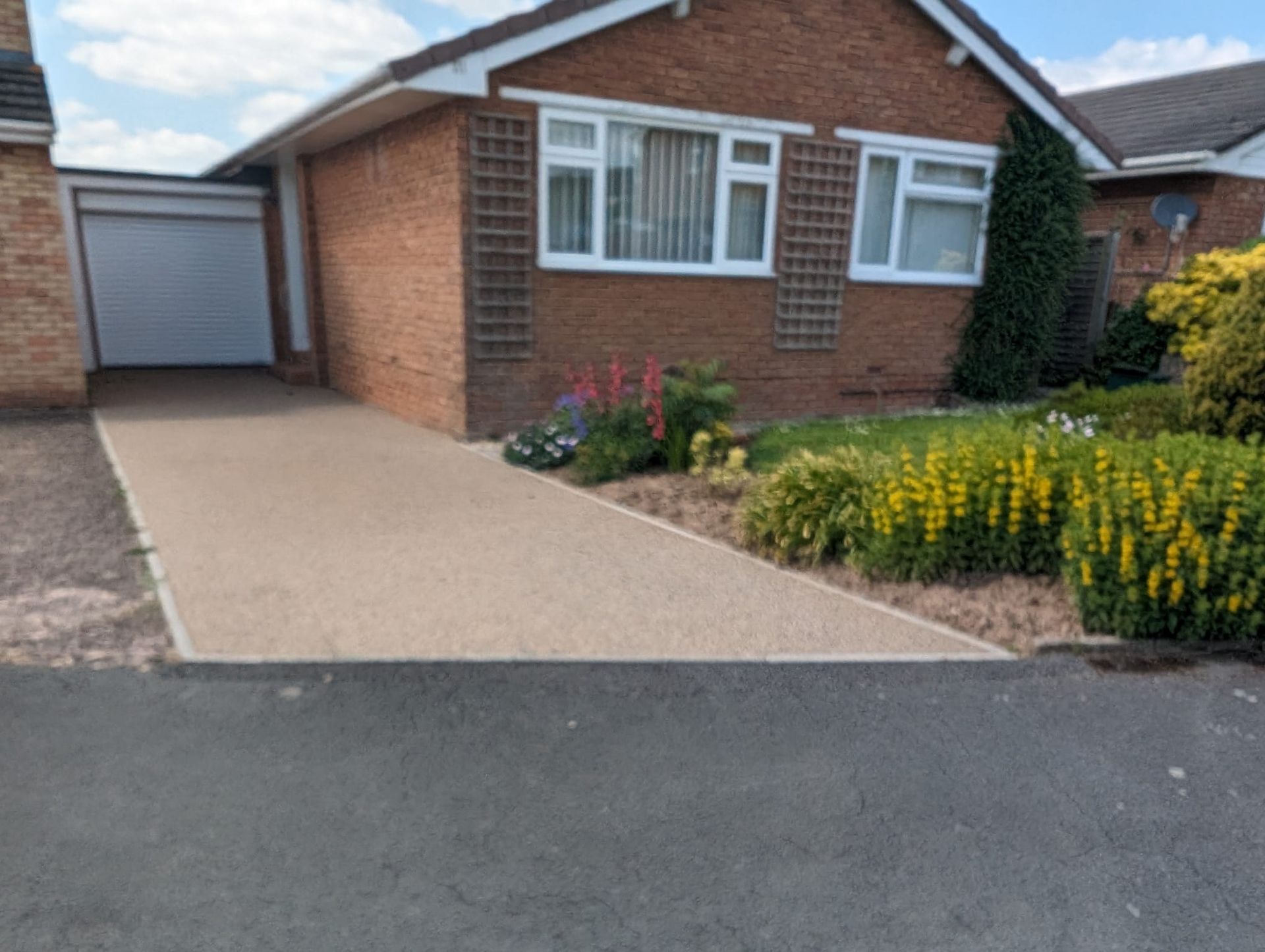 DIY resin driveway in a gold colour, with a red brick house in the background.