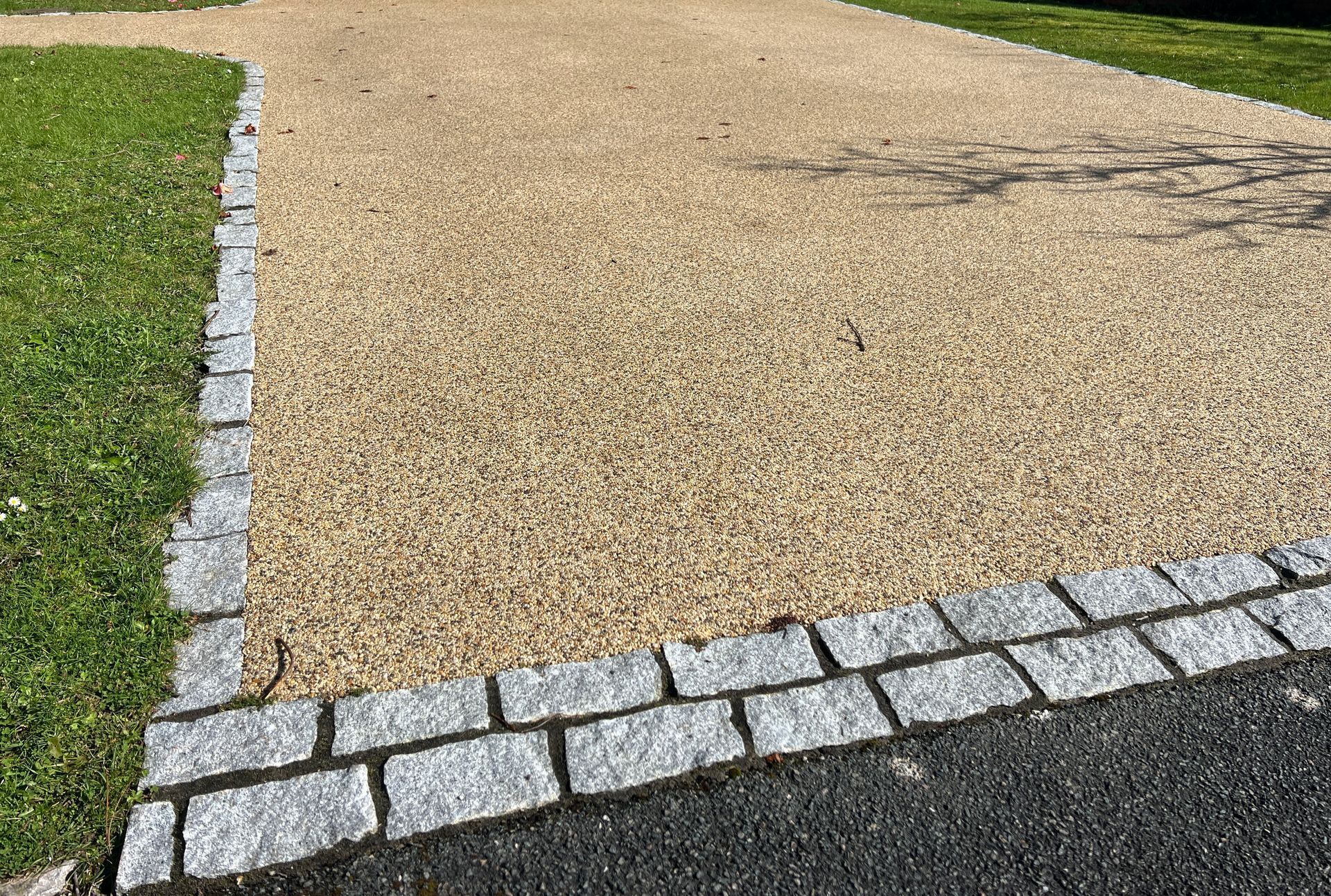 Gravel driveway bordered by stone blocks and grass.
