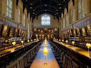 A long dining hall with tables and chairs and lamps.