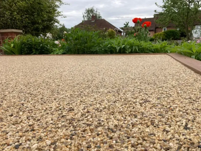 Large resin bound driveway area in a golden brown colour, with greenery on the side.