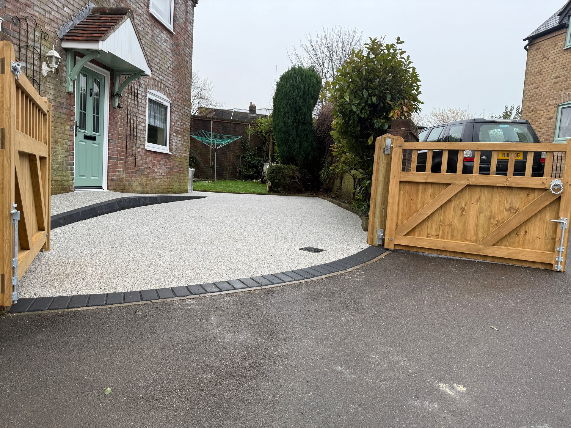 Driveway with white gravel, wooden gates, and a brick house with a green door.