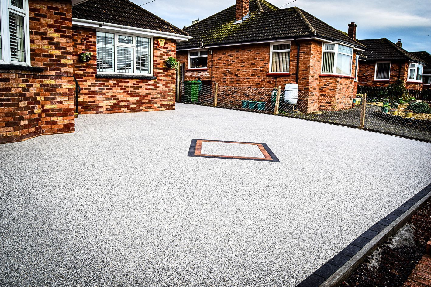 Grey resin driveway in front of a red brick bungalow.