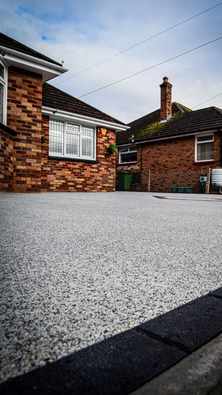 Brand-new grey resin driveway with a diamond shape in the middle made from block paviours.