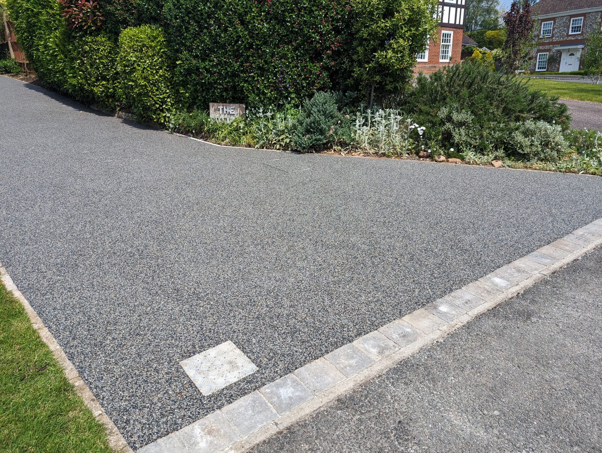 Grey resin driveway with green plants around it, and grey blocks on the front.
