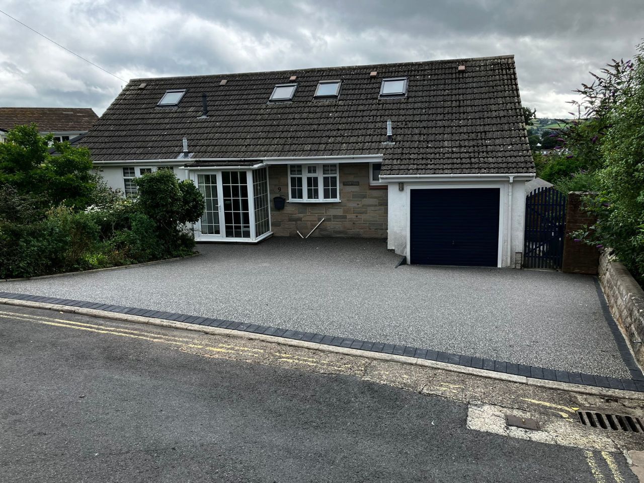 Dark grey resin driveway with black block paviour edging.
