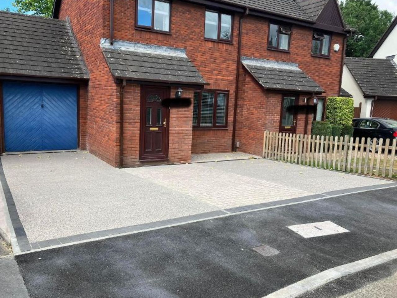 Light grey resin driveway with a blue garage door and red brick house in the background.
