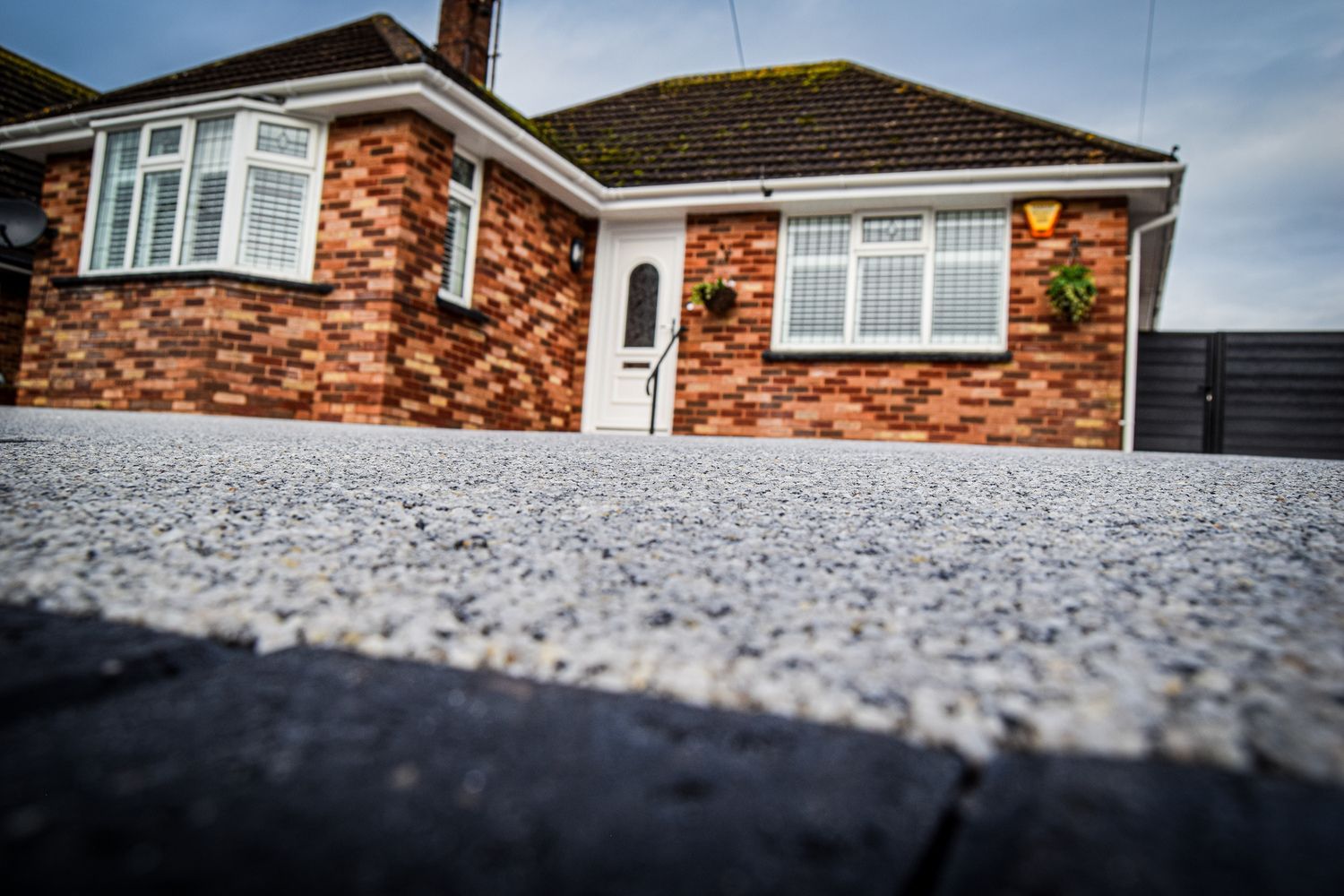 Resin driveway in a grey colour with a red bungalow in the background.