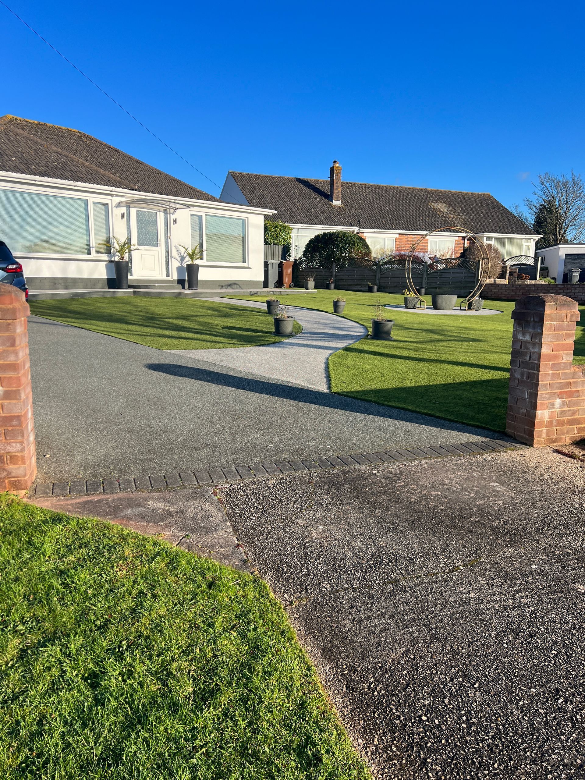 A house with a gravel driveway, a lawn with garden features, and a blue sky.