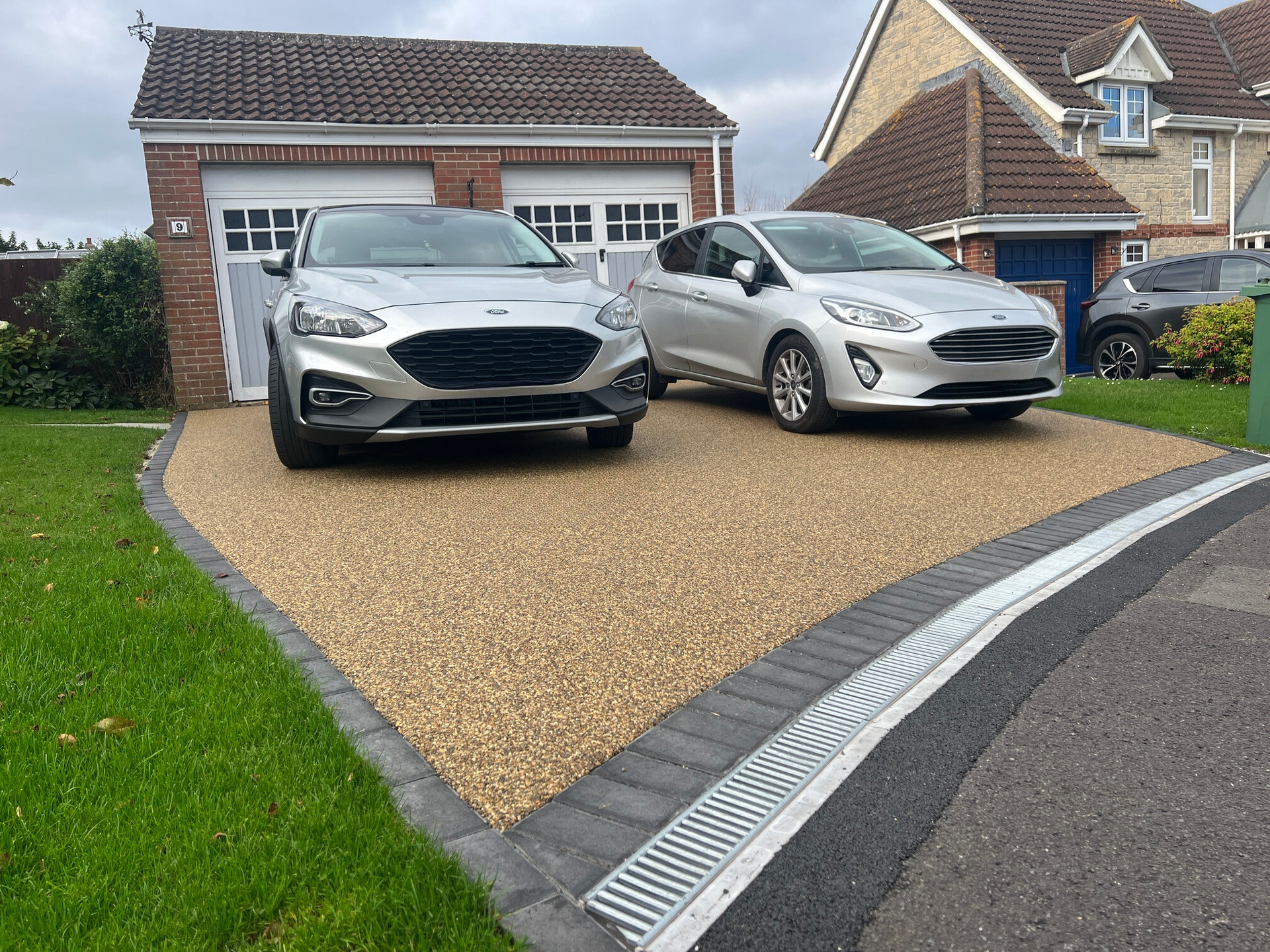 Two silver cars parked on a gravel driveway in front of a garage and a house.