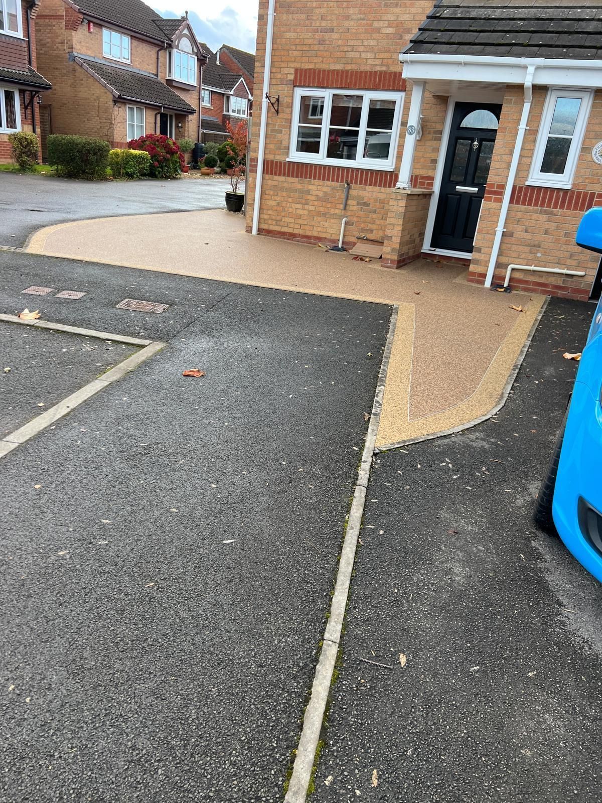 Driveway with asphalt and tan paving leading to a brick house with a black door.