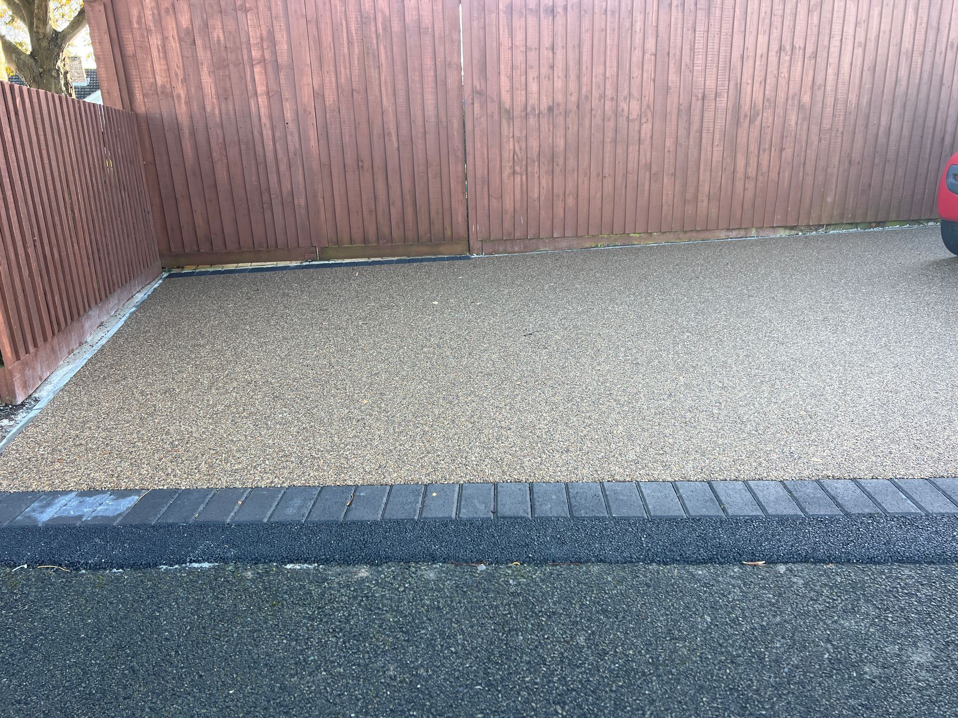 A gravel driveway with a black brick border and brown wooden fence.