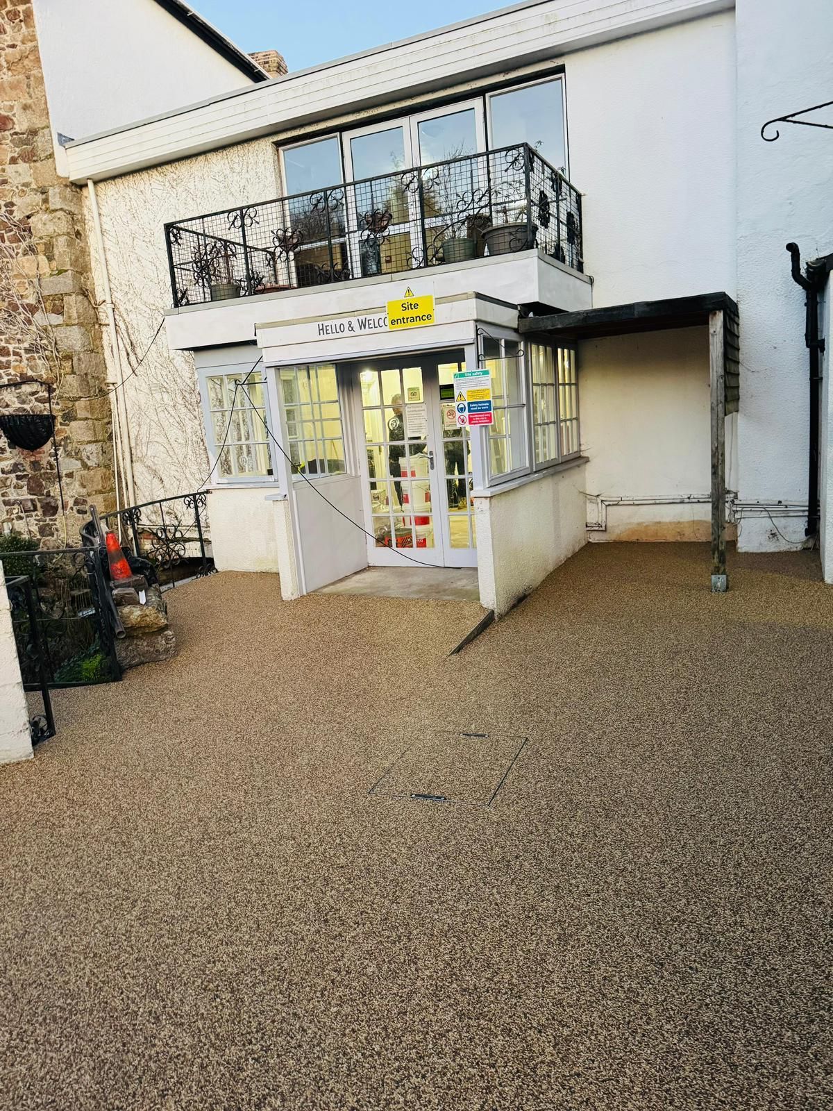 Exterior of a white building with a balcony and a covered entrance. Gravel driveway leads to the door.
