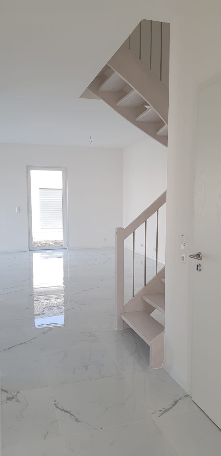 Innenansicht eines modernen weißen Hauses mit Treppe und großem Marmorboden.