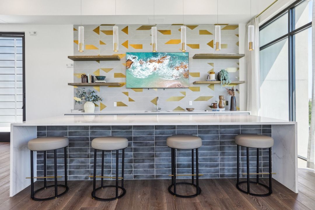 Coworking kitchen and coffee bar with counter stools and a patterned tile backsplash.