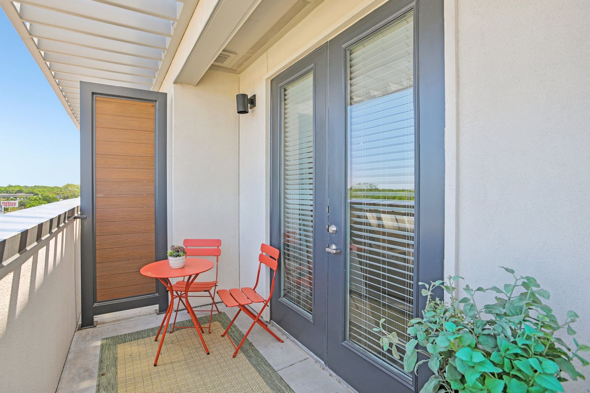 Balcony with red table and chairs, potted plant, and glass doors.